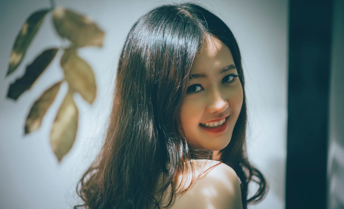 Portrait of a beautiful Asian woman with long hair smiling warmly, captured in an elegant studio setting.