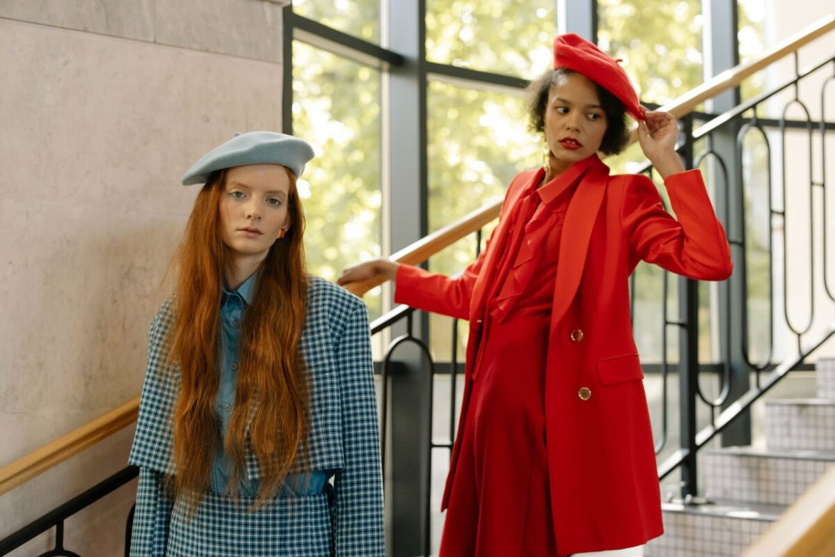 Two women in fashionable outfits pose stylishly outdoors by a staircase.